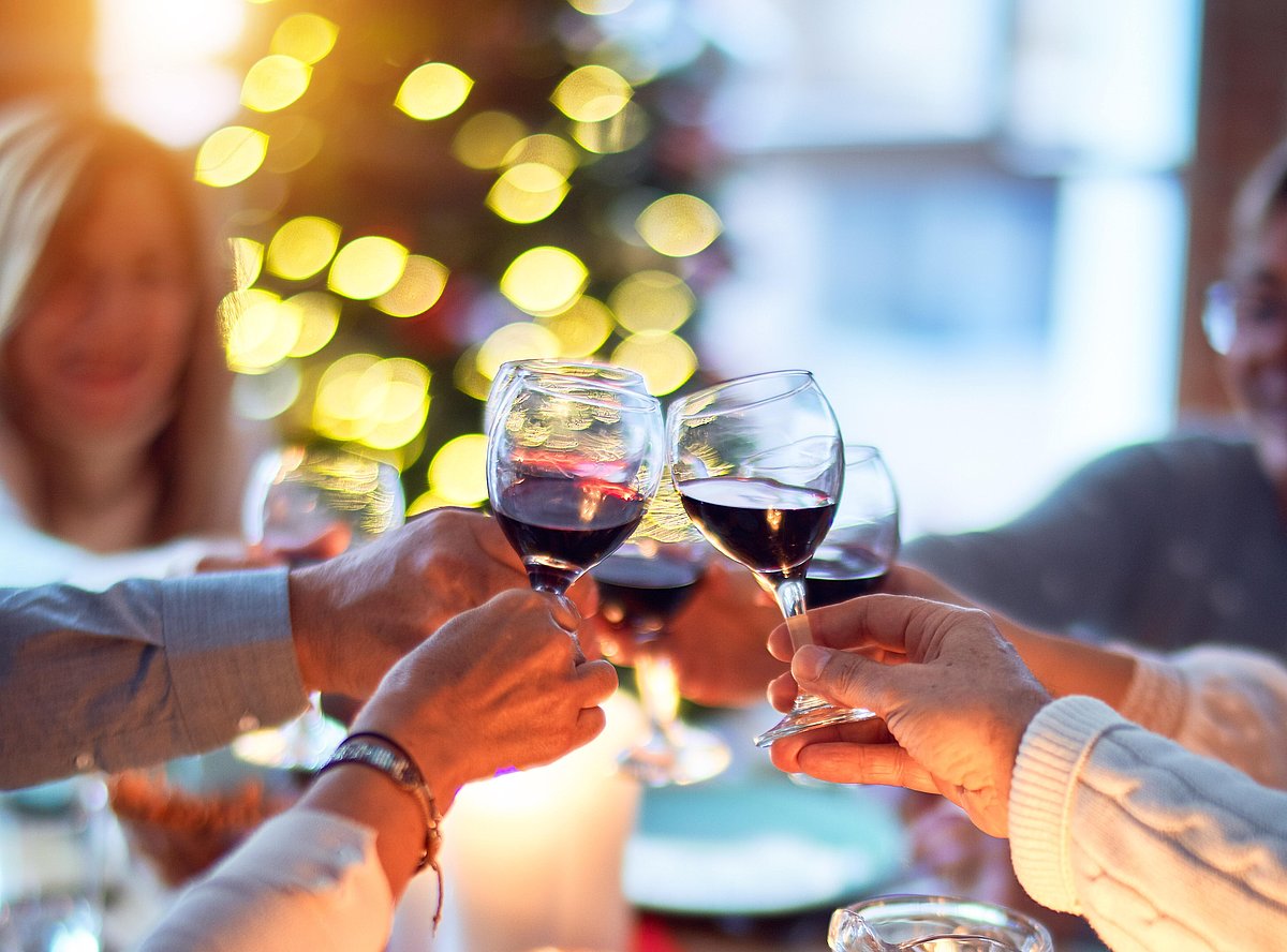 Mehrere Personen stoßen mit Wein an; im Hintergrund ist es weihnachtlich dekoriert