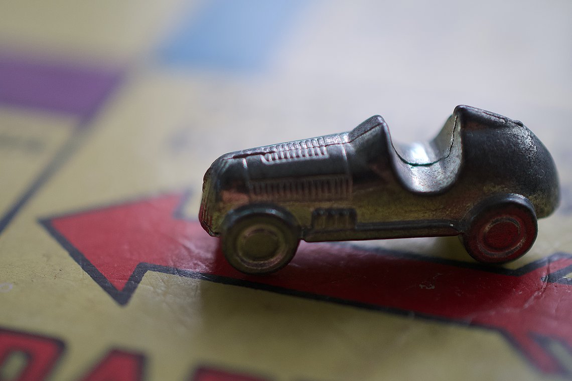 Die Spielfigur "Auto" aus dem Spiel Monopoly steht auf dem Los-Feld